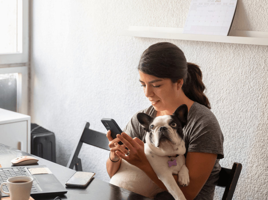 A sitting down, holding a dog in her arms while reading a text on her phone.